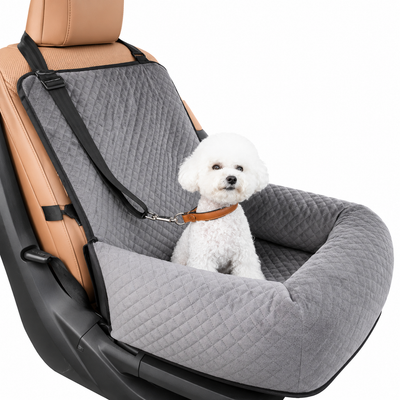 A small white dog sits inside a gray quilted pet car seat cover installed on a tan car seat, with a leash attached. The product is shown on a clean white background.